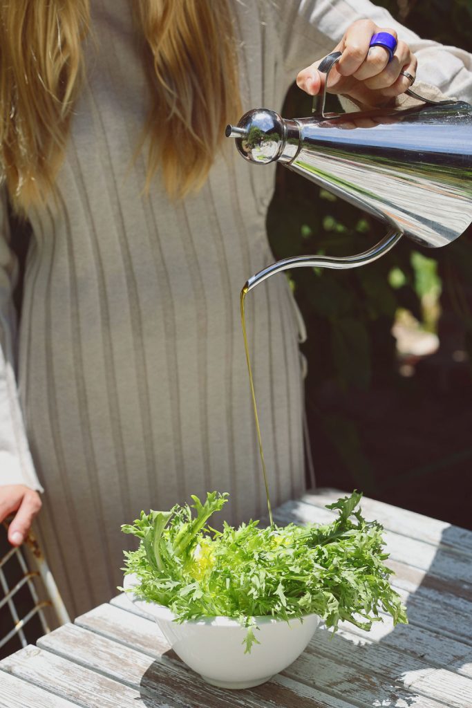 Elle-Lou pouring oil from jug into a bowl of greens