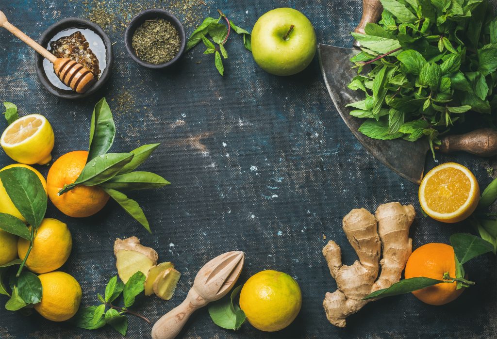 Ingredients for making natural hot drink. Oranges, fresh mint, lemons, ginger, honey, apple and spices in bowl over plywood background, top view, copy space. Clean eating, detox, dieting concept
