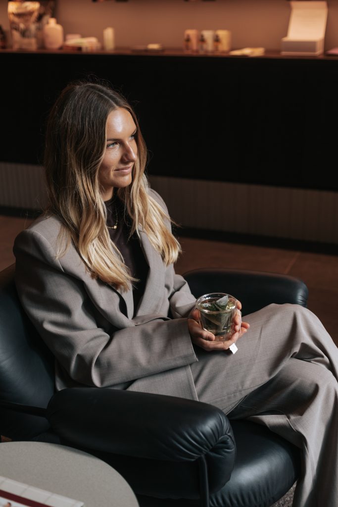 Elle-Lou holding tea, sitting on chair looking ahead. 